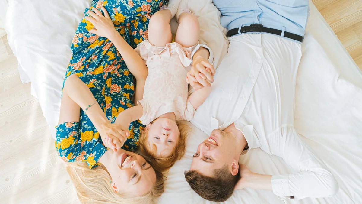 A family of three lying on a bed, with the mother, father, and baby positioned in a way that suggests they are relaxing together.