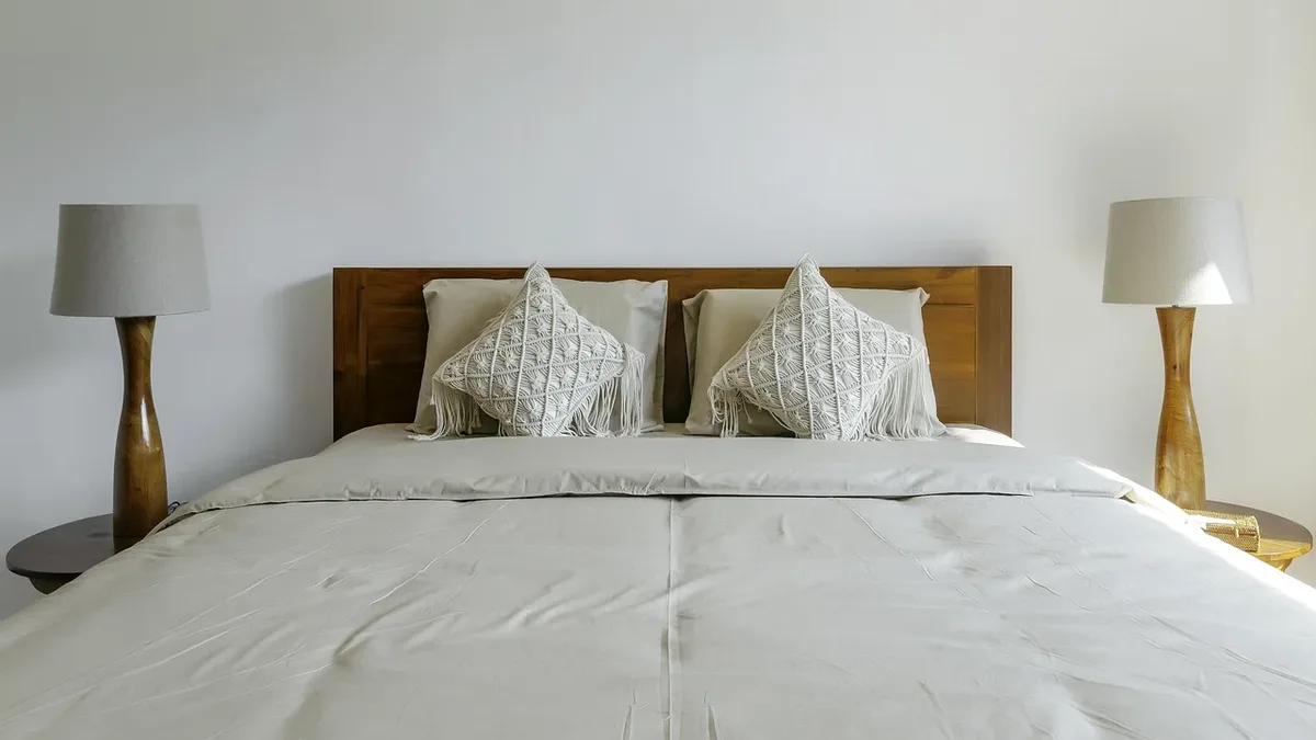 A bed with a white comforter and pillows, two lamps on either side of the bed, and a white wall behind the bed.