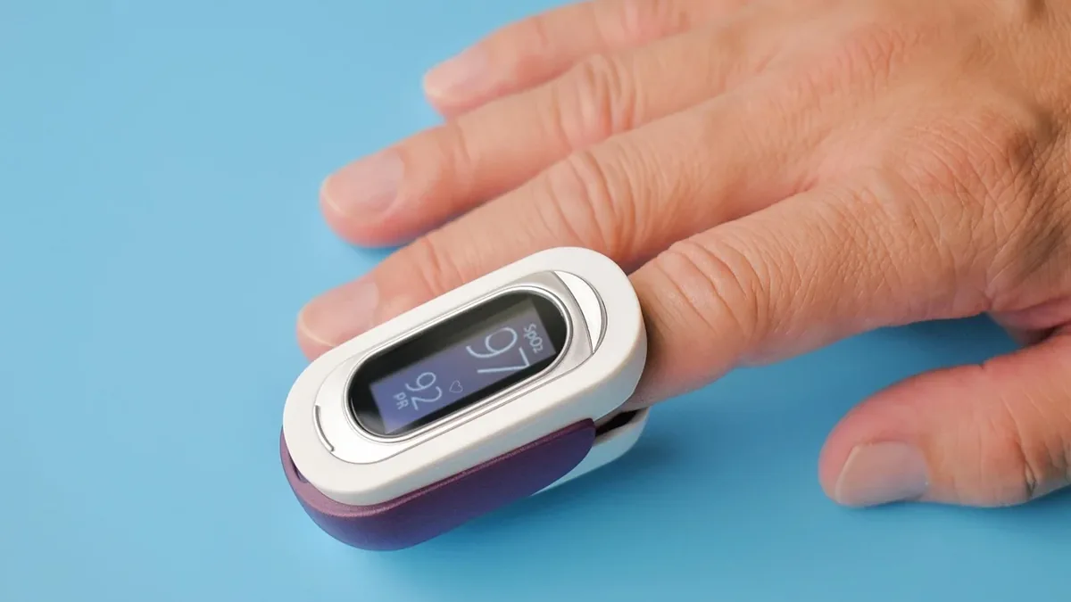 A person's hand with a pulse oximeter attached to the middle finger.