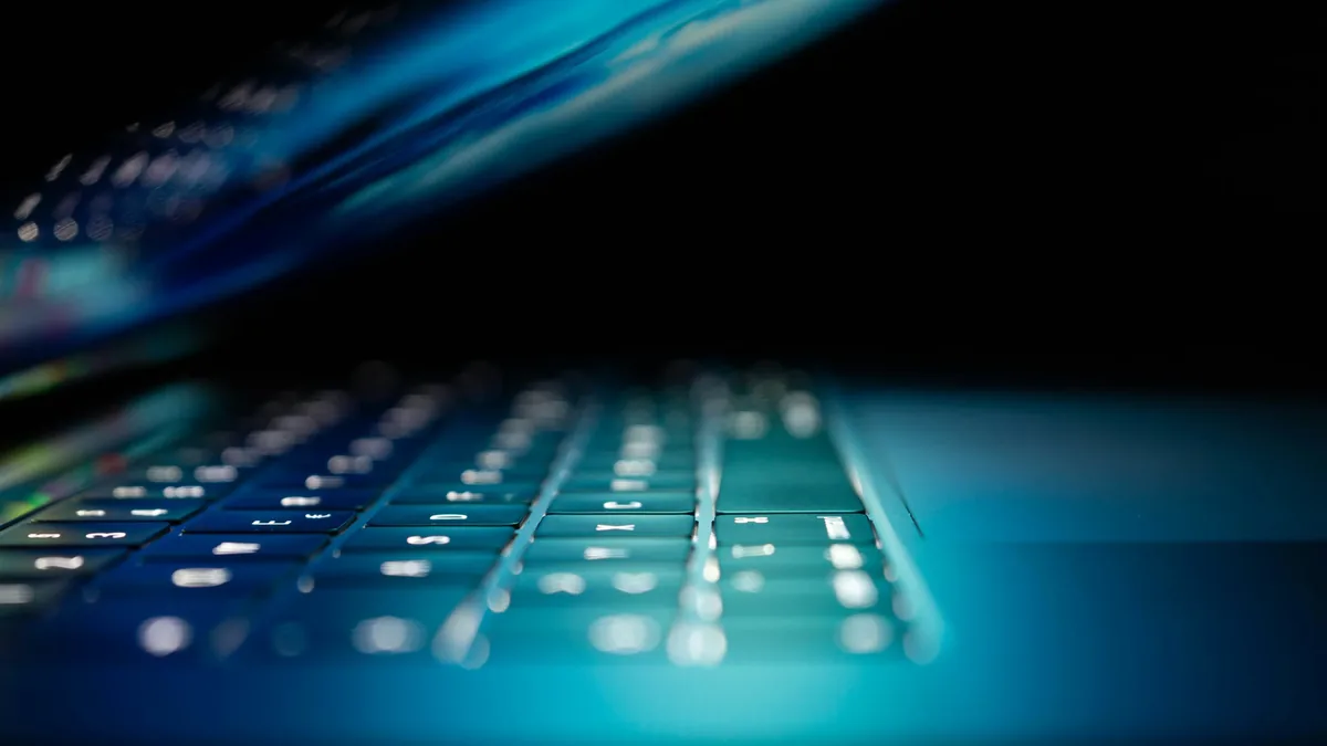 A close-up view of a laptop keyboard, with the keys and surrounding area illuminated by a blue light.