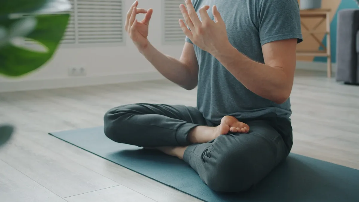 A person sitting cross-legged on a yoga mat, with their hands raised in a meditative pose.