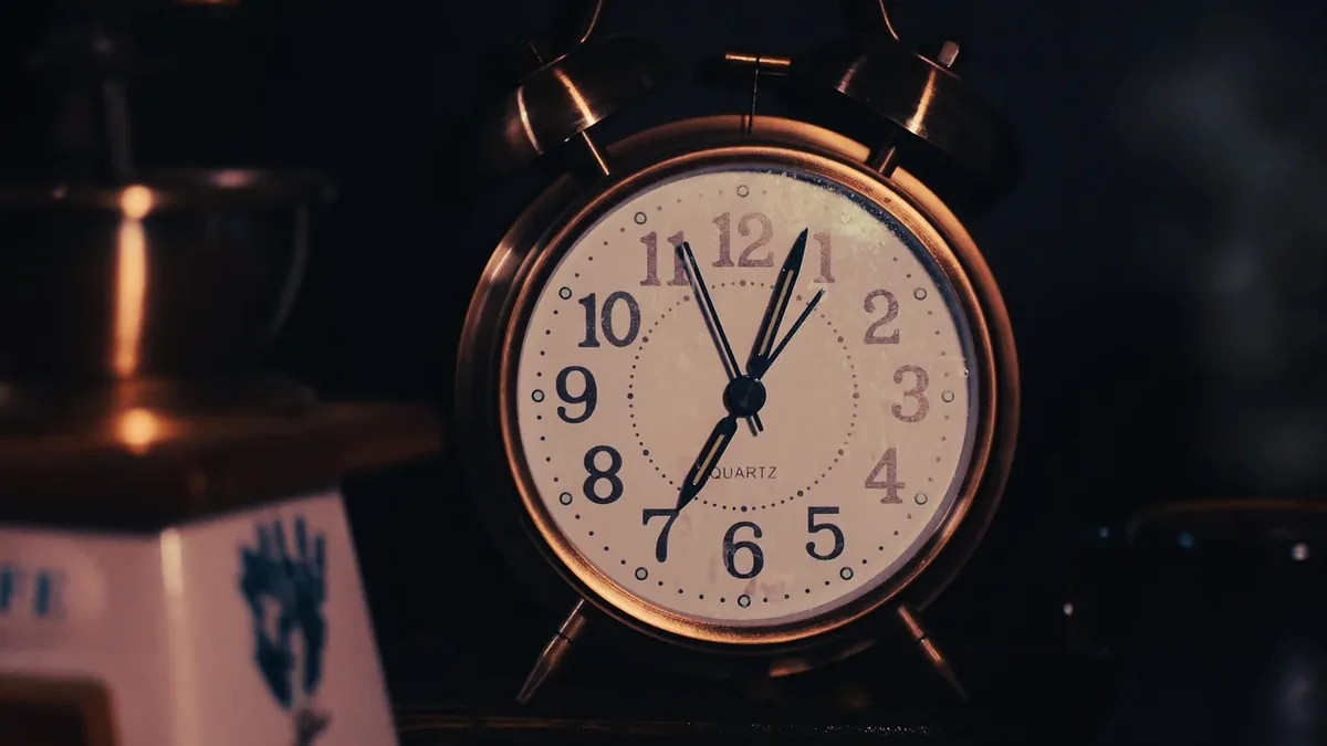 An alarm clock with a white face and black hands, set to 10:10, sitting on a dark surface.