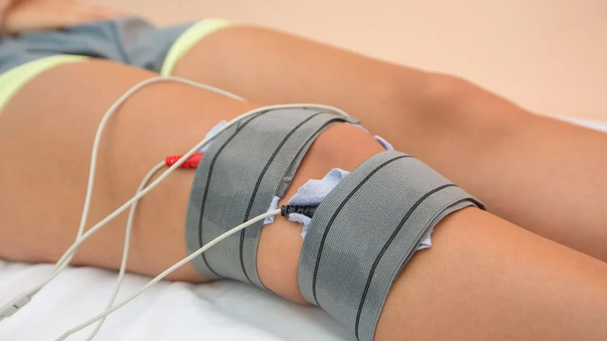 A person lying on their back with their legs wrapped in gray straps and wires attached to their legs.