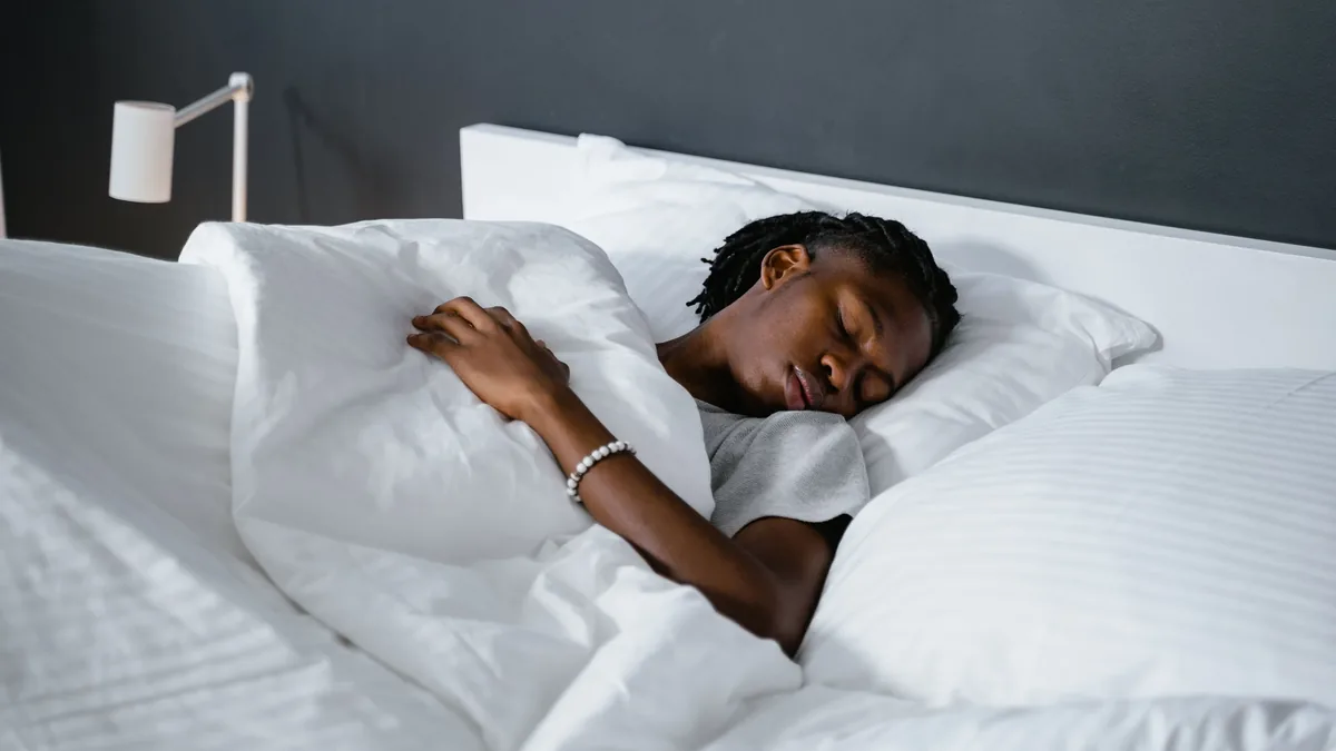 A person sleeping in a bed with white sheets and pillows, lying on their side with their head resting on a pillow and their arm bent at the