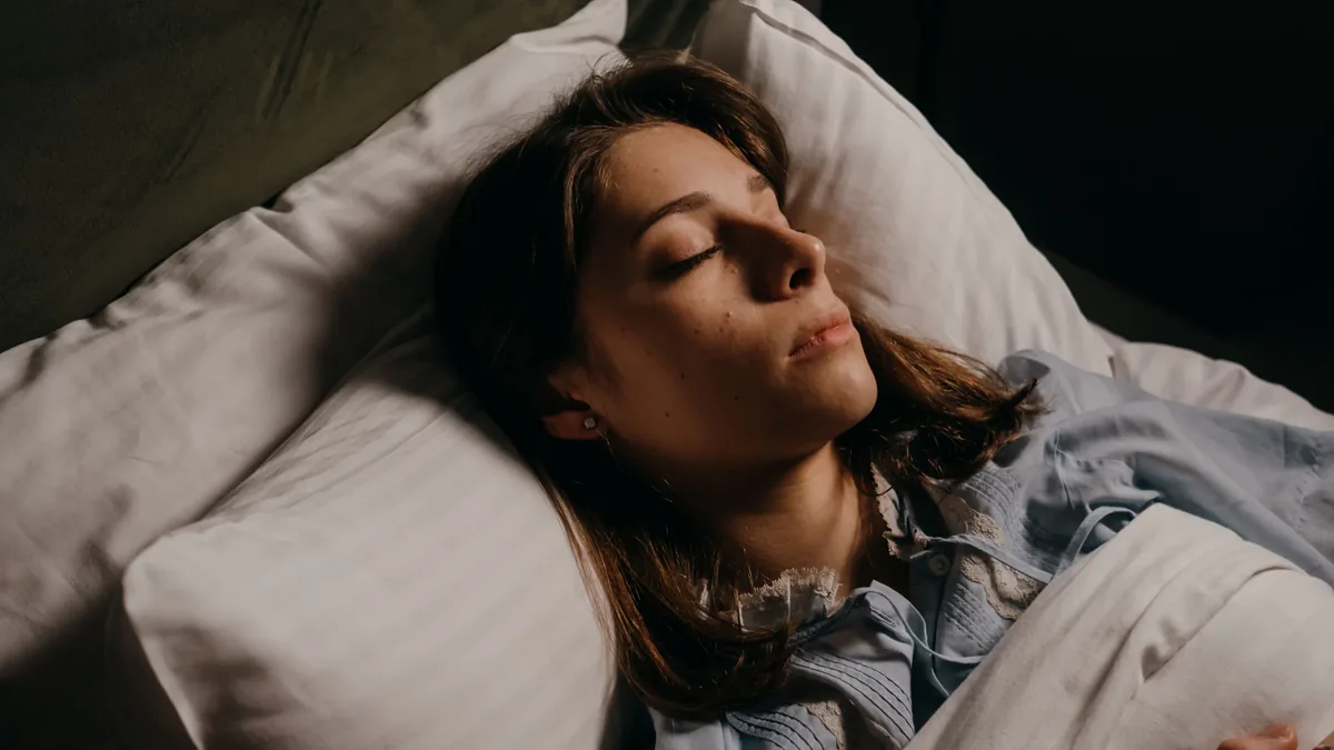 A woman sleeping in bed, with her head resting on a pillow and her body covered by a blanket.