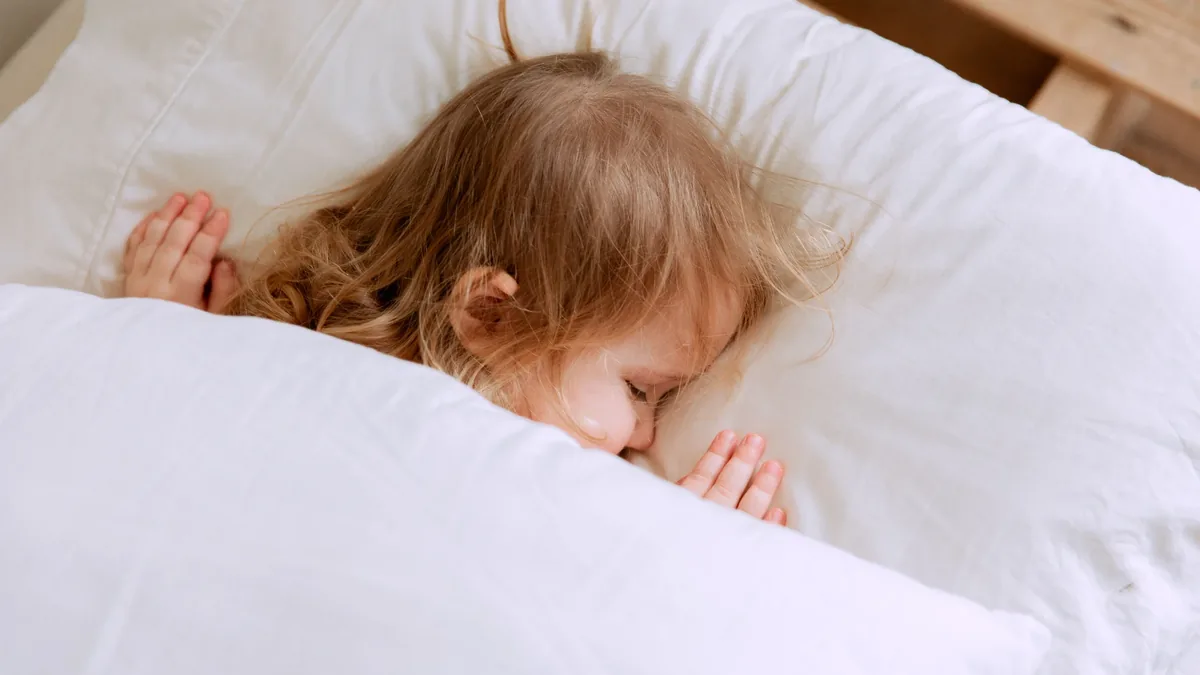 A young girl sleeping in bed, surrounded by white pillows and sheets.