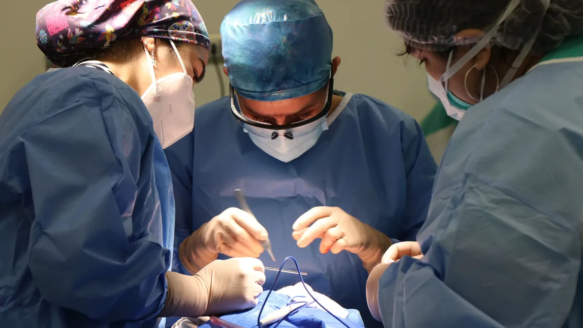 Three surgeons are shown performing surgery on a patient, with the surgeons wearing blue scrubs and surgical masks, and the patient's body p