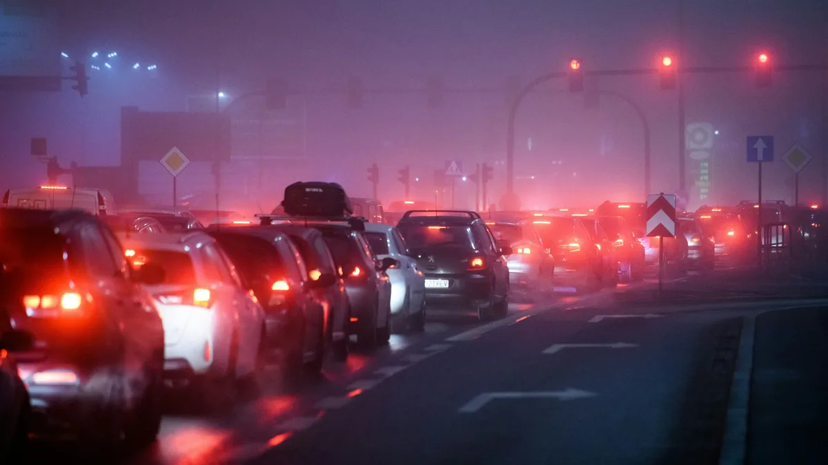 A nighttime scene of a busy road with multiple cars, each featuring red brake lights, driving in the same direction, with a few vehicles stopped at a red light.