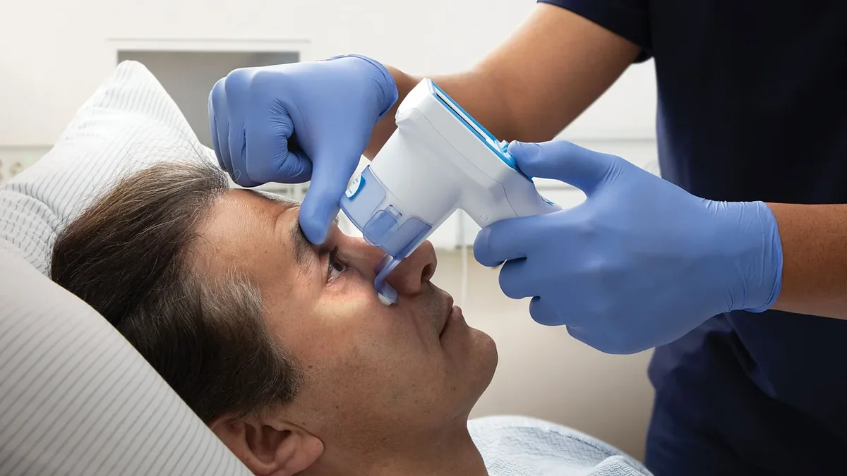 A person lying on a bed with a medical professional standing over them, holding a device to the person's face.